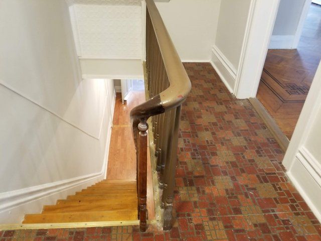 A staircase with a wooden railing and a brick floor