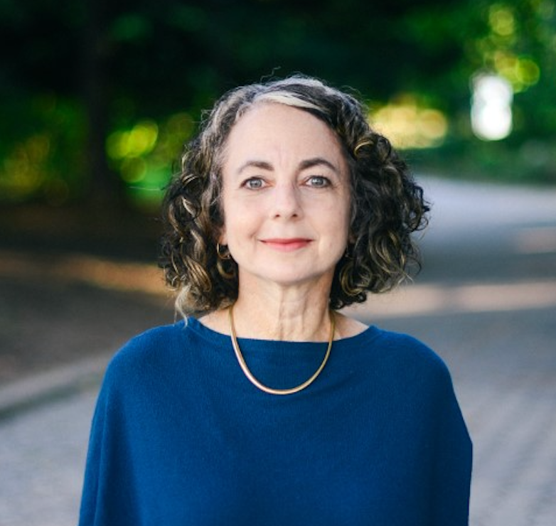 A woman with curly hair is wearing a blue sweater and a gold necklace.