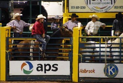 A group of cowboys are riding a bull in a rodeo arena sponsored by aps