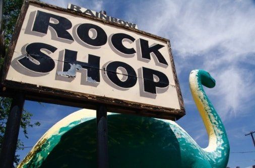 A sign for the rock shop with a dinosaur statue in front of it