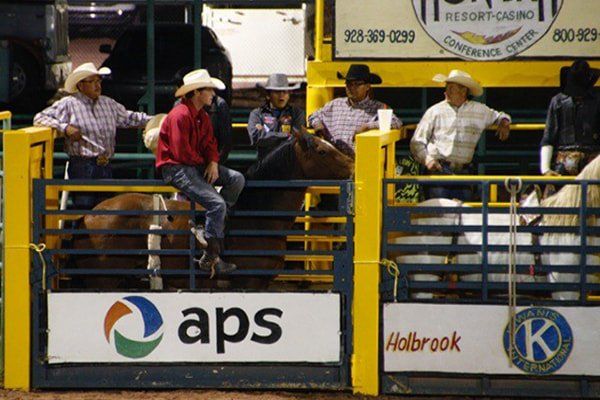 A man riding a horse in a rodeo arena with a sign that says aps