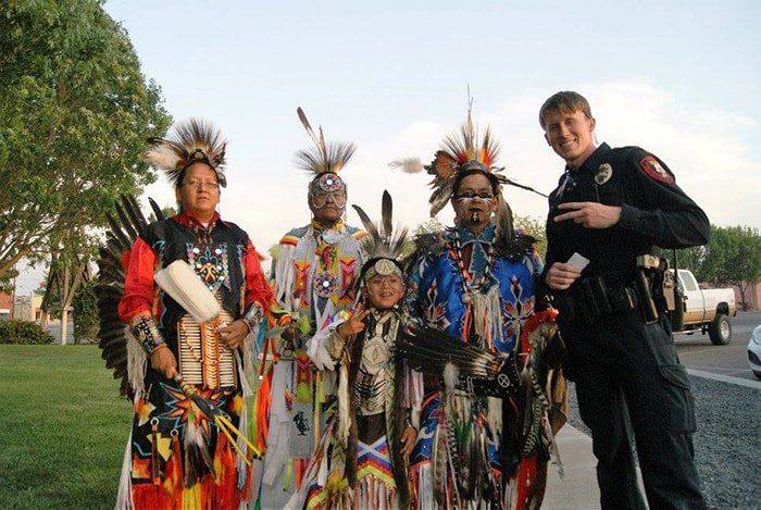 A group of people in native american costumes are posing for a picture with a police officer.