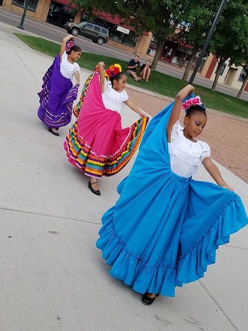 Three girls in colorful skirts are dancing on a sidewalk