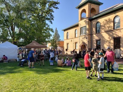 A group of people are standing in a grassy field in front of a large building.