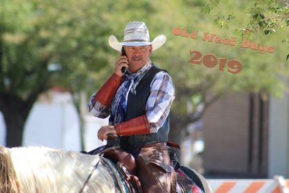 A man in a cowboy hat is riding a horse and talking on a cell phone.