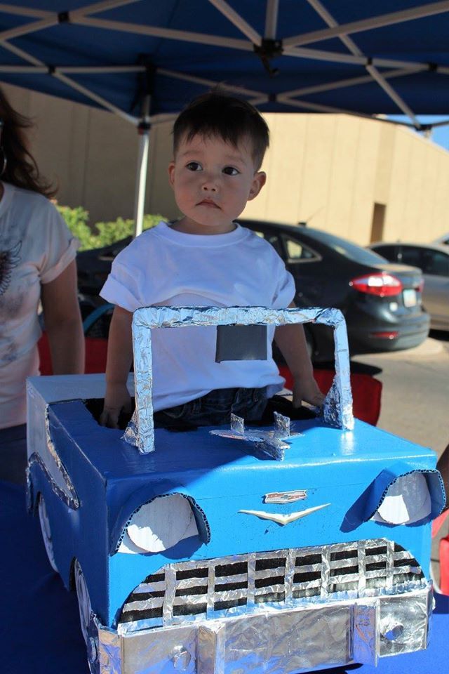 A little boy is sitting in a cardboard car