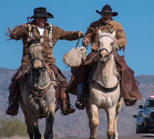 Two men are riding horses down a road.