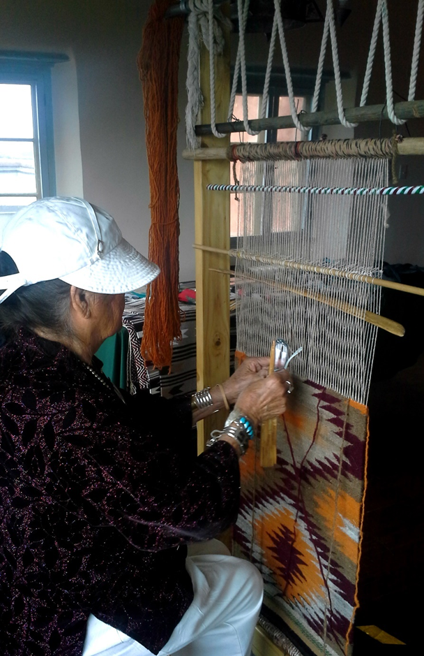 A woman is weaving a rug on a loom.