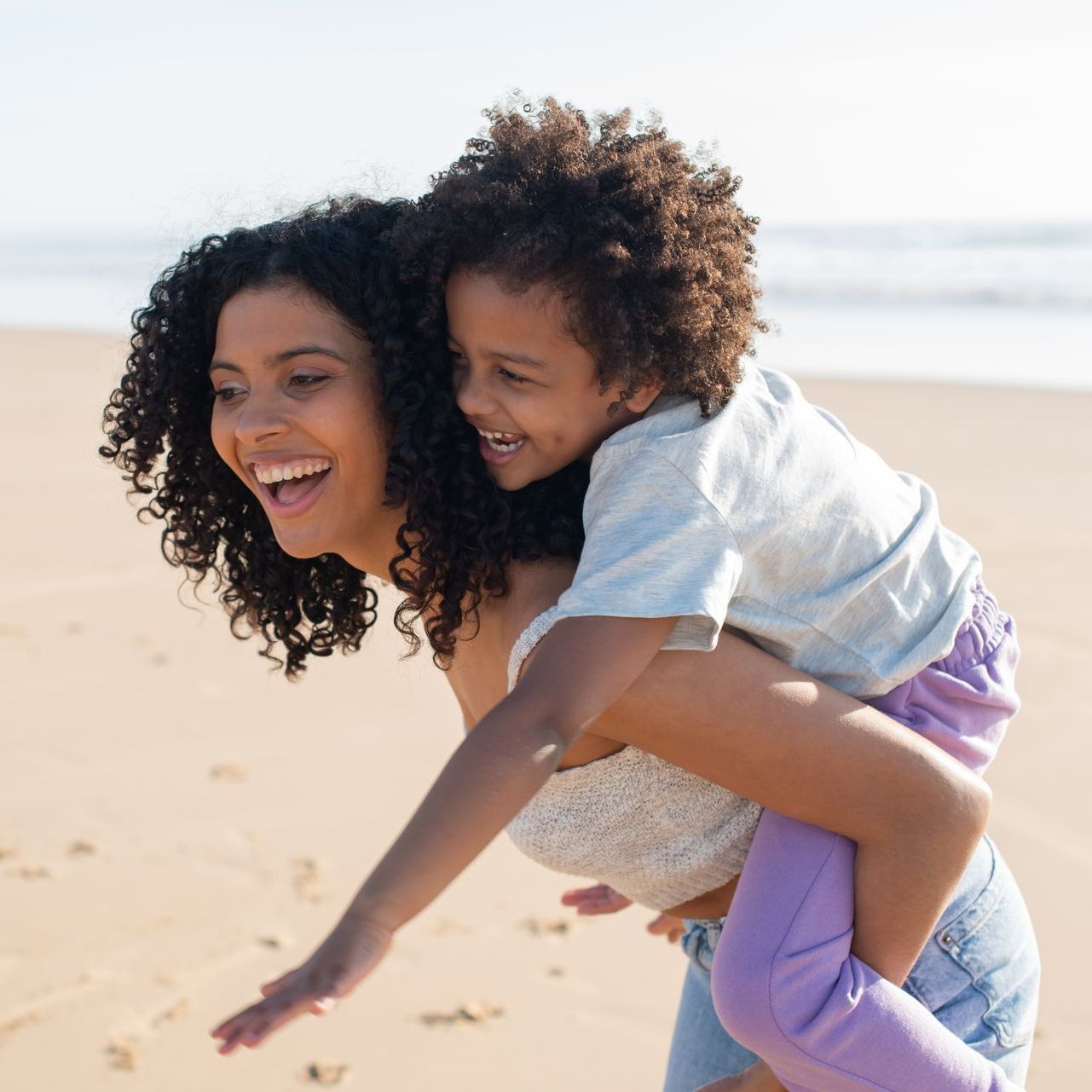 A woman is giving a child a piggyback ride on the beach