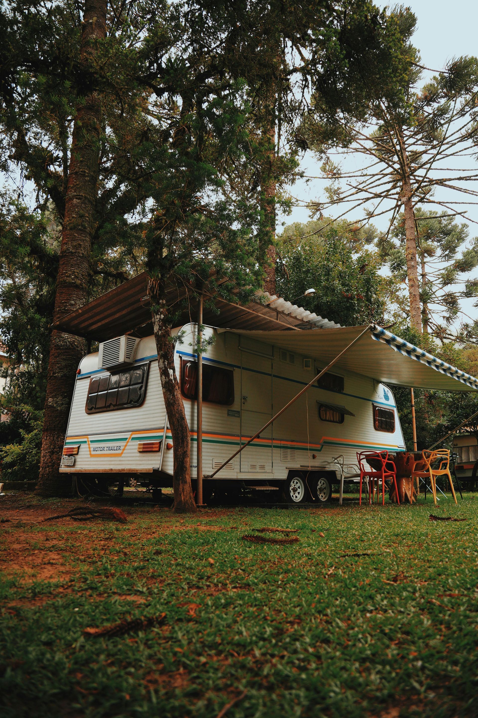 A rv with a canopy is parked in a grassy field.