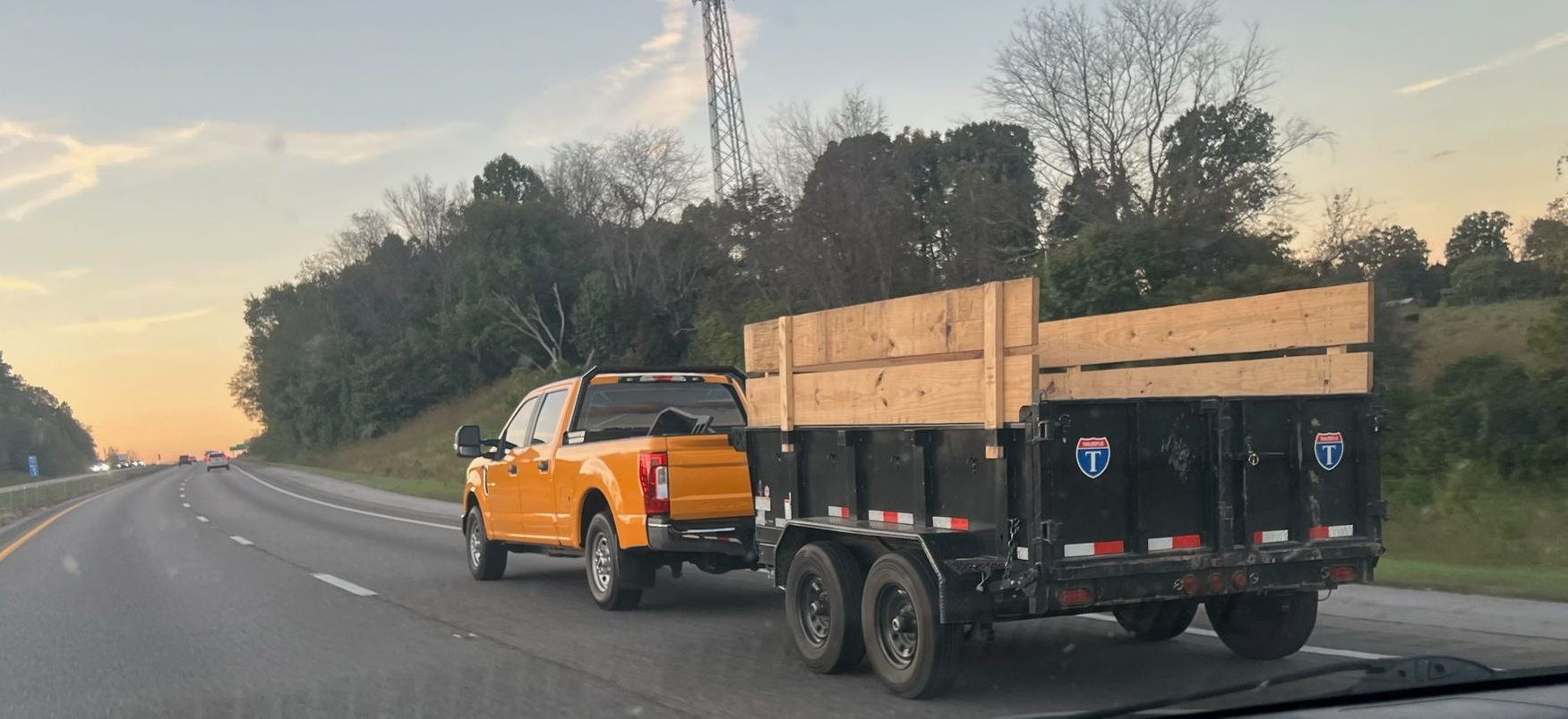 Basketball hoop on a grassy hill with tire bases and a nearby building under a blue sky.