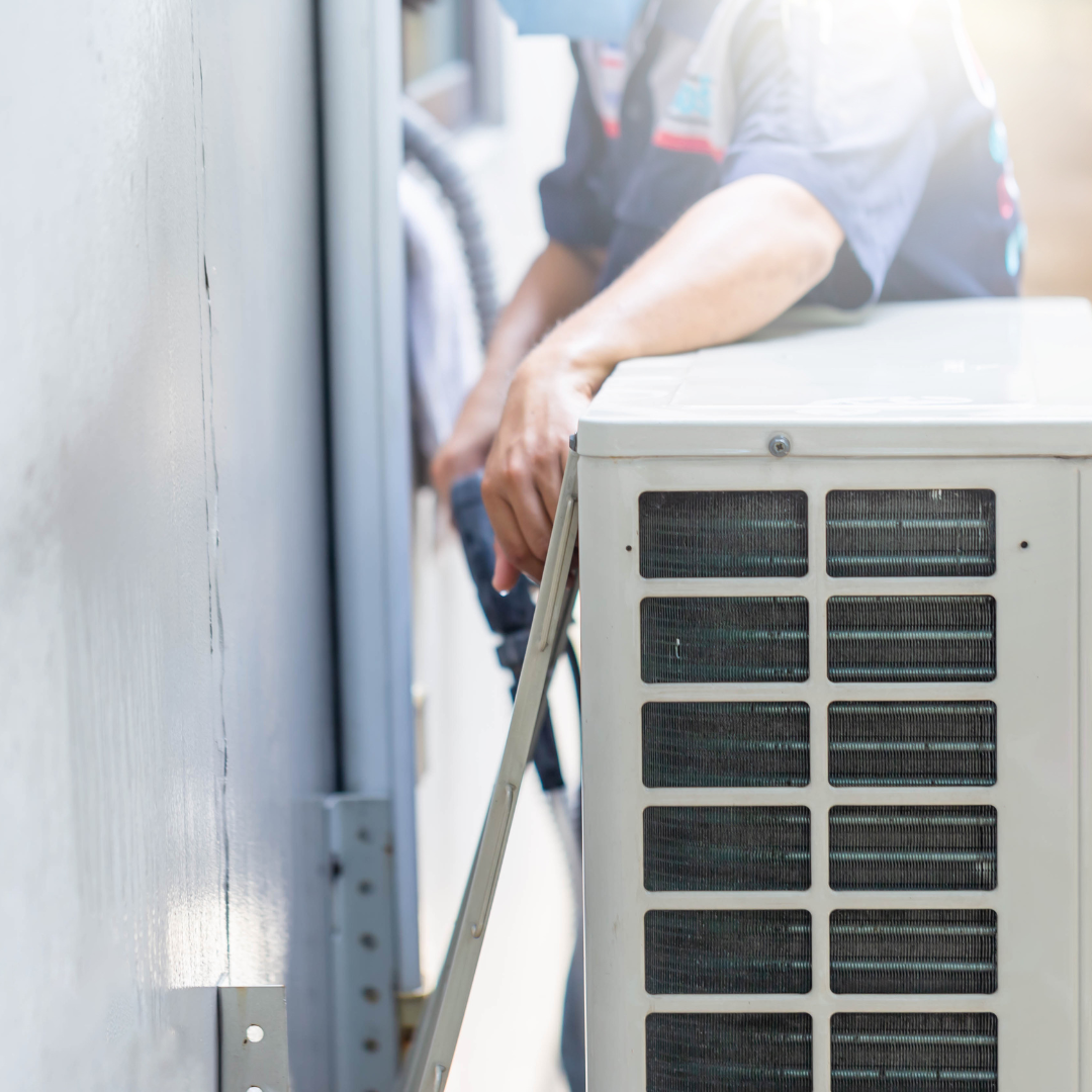 A man is working on an air conditioner outside of a building.