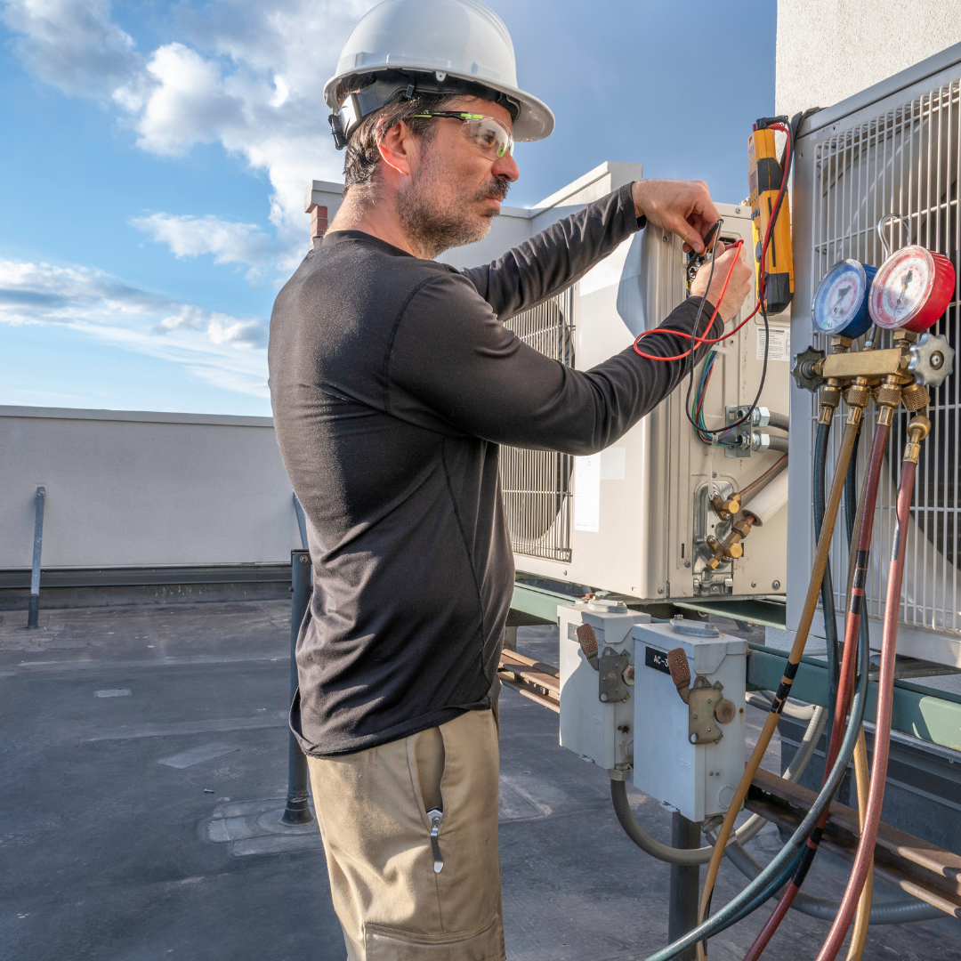 A man wearing a hard hat and safety glasses is working on an air conditioner.