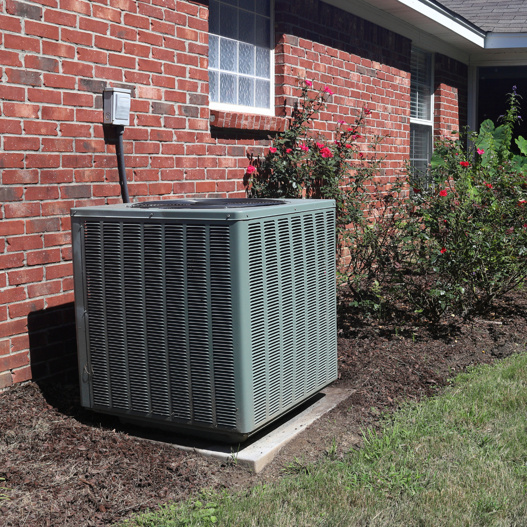 An air conditioner is sitting outside of a brick house