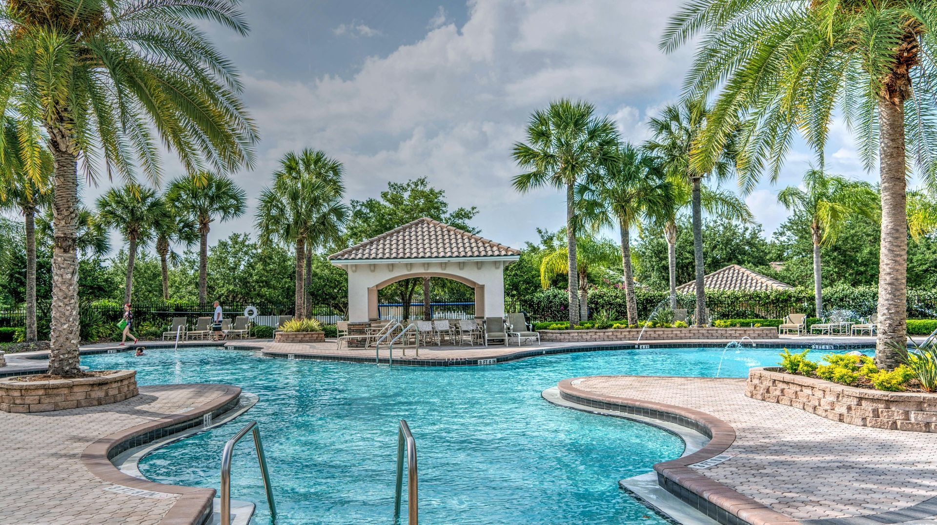 A large swimming pool surrounded by palm trees and a gazebo.