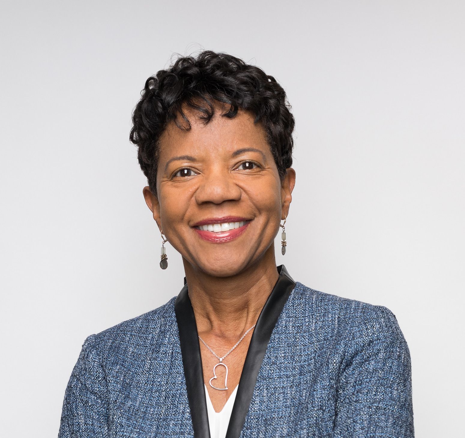 A woman wearing a blue jacket and earrings is smiling for the camera.