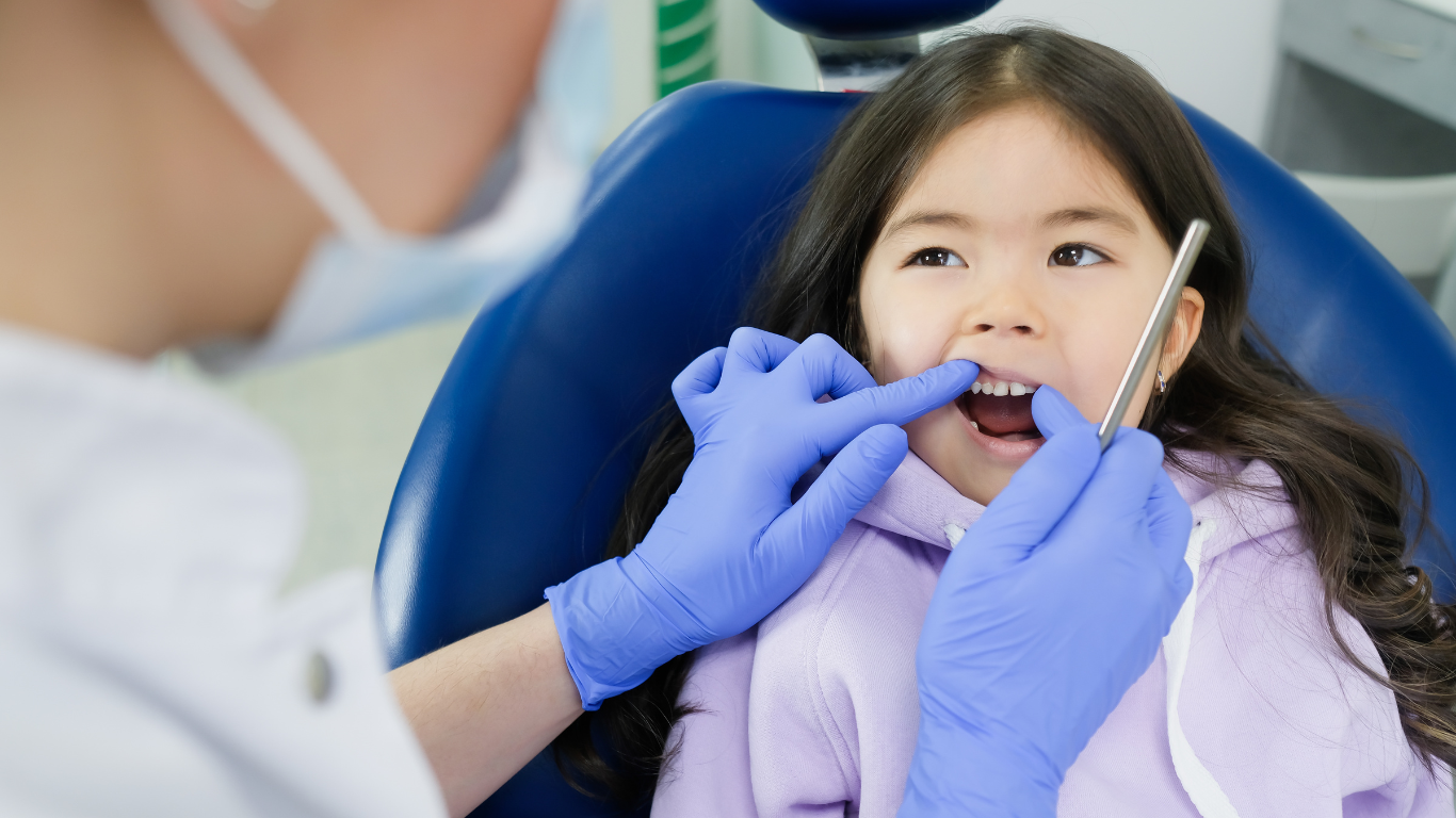 Man at dentist, mouth open, being examined with tools by gloved hands.