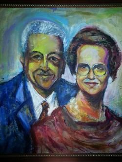 Portrait of a smiling couple: man in a blue suit, woman wearing glasses and a red top.