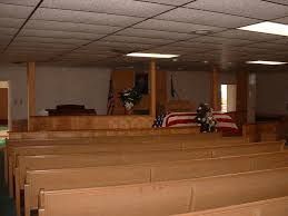 Funeral home interior with rows of pews facing a casket draped with a flag.