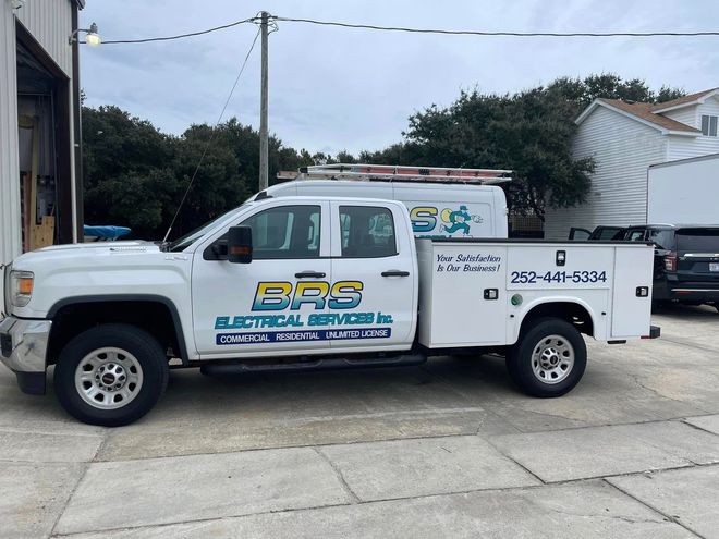 A white electrical truck is parked in front of a building.