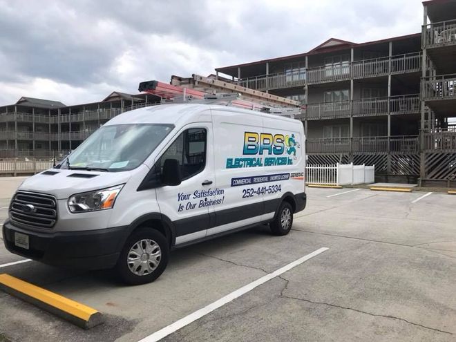 A white van is parked in a parking lot in front of a building.