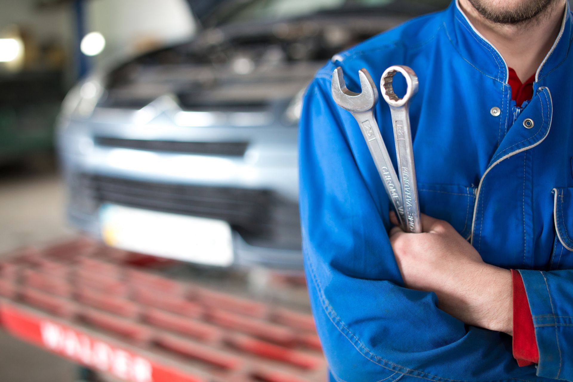 A mechanic is holding wrenches in front of a car | Beer's Automotive Services and Repair