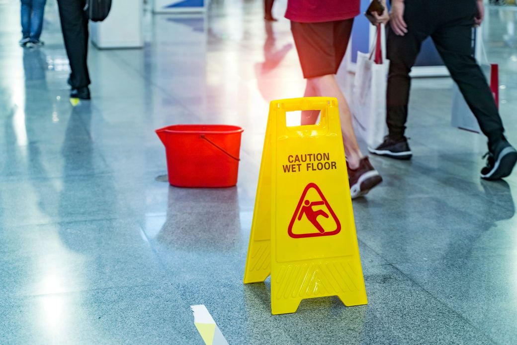 A yellow caution sign is sitting on the floor next to a red bucket.