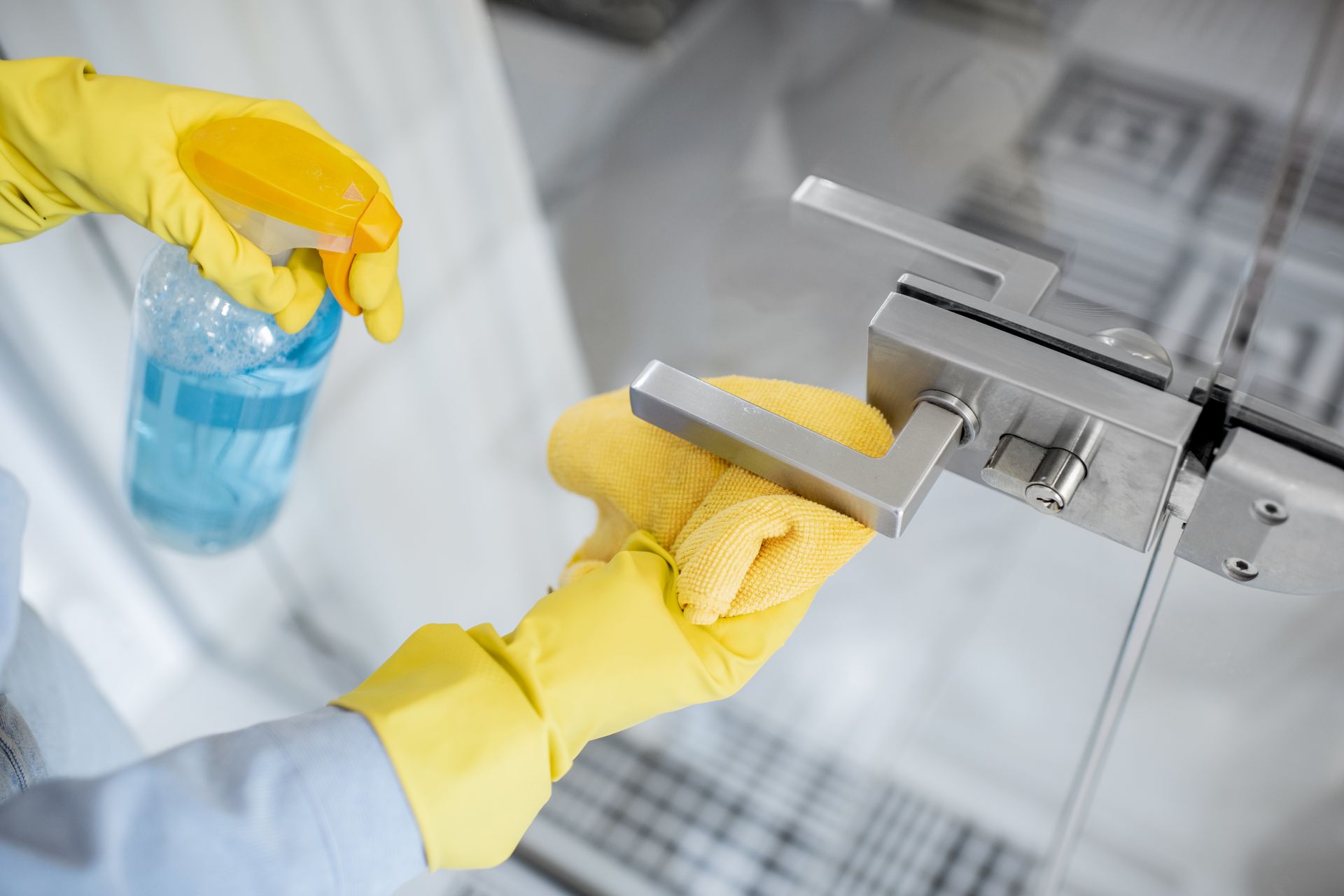 A person wearing yellow gloves is cleaning a door handle with a spray bottle.