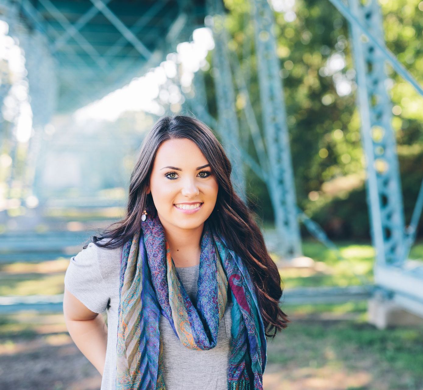 A woman wearing a scarf and a gray shirt is standing under a bridge.