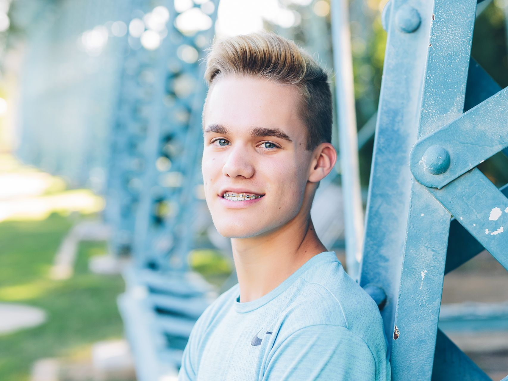 Teenager with braces smiles, leaning against a blue metal bridge.