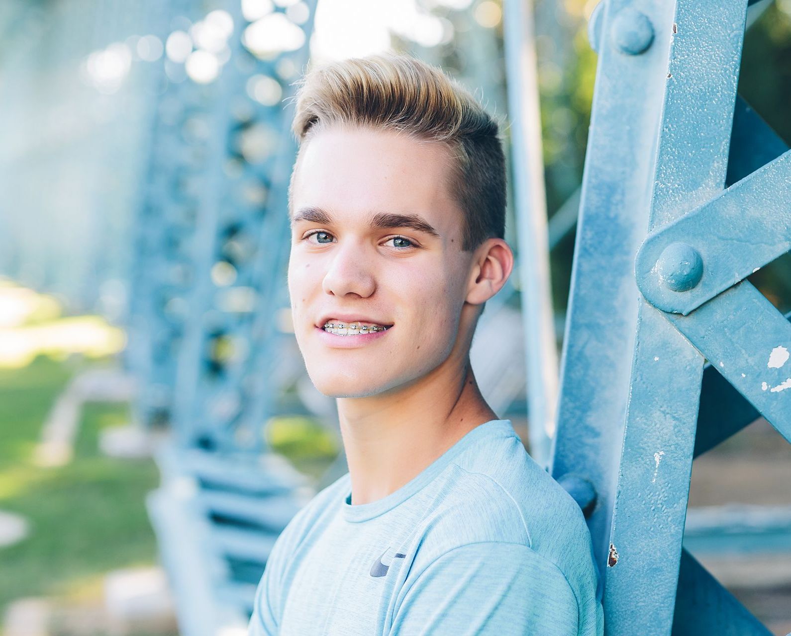 A young man in a blue shirt is leaning against a metal structure.