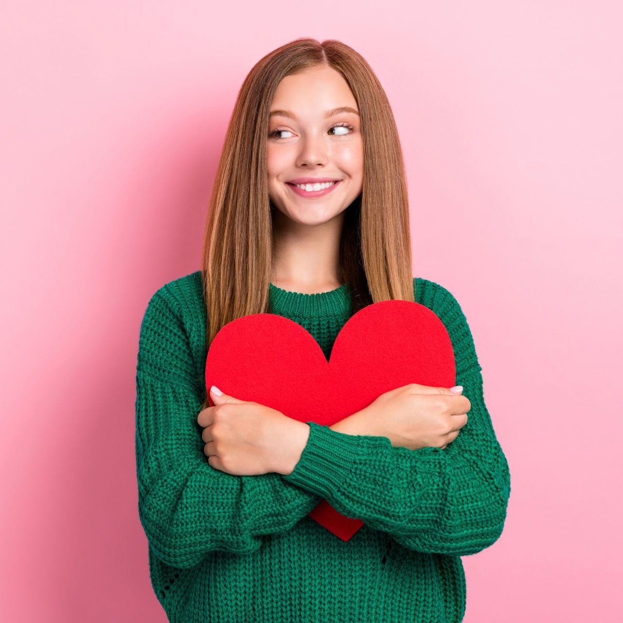 A young woman in a green sweater is holding a red heart.