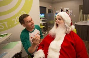 A man is feeding santa claus a spoon in a dental office.