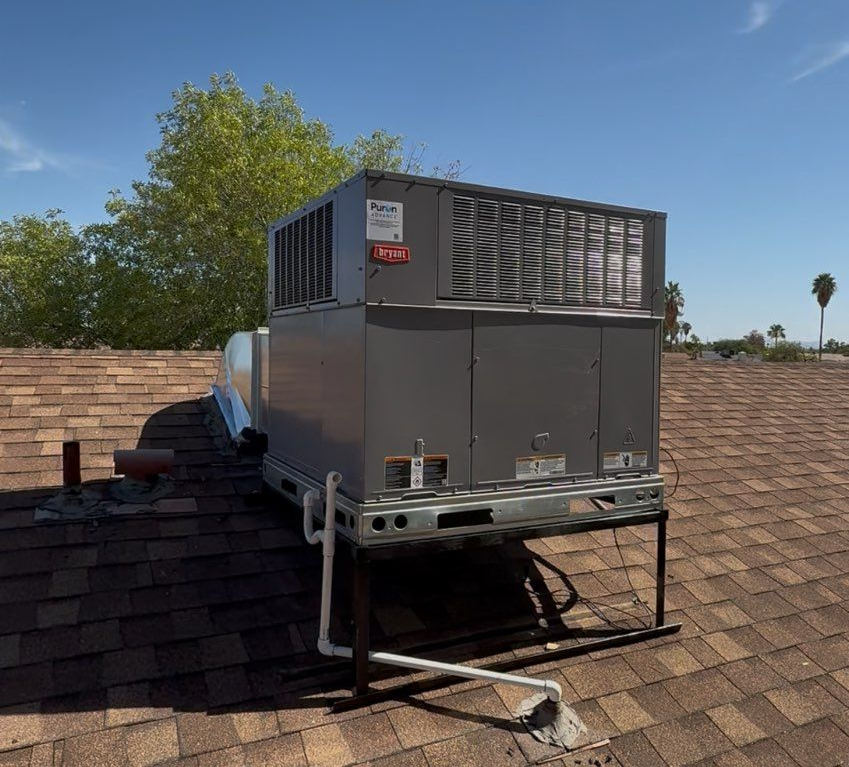 Rooftop HVAC unit, gray, on brown shingles, bright sunny day.
