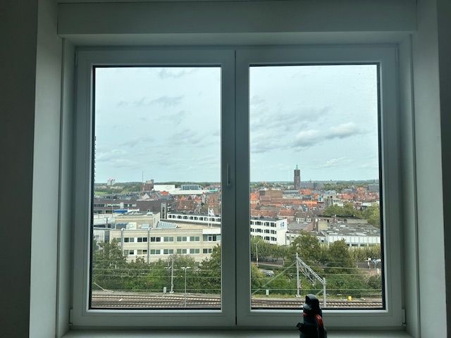 Uitzicht op een stadsgezicht door een raam. Bewolkte lucht boven gebouwen, spoorlijnen en een kerktoren in de verte.