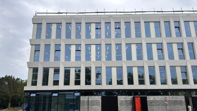 Modern wit gebouw met rechthoekige ramen en een bewolkte hemel op de achtergrond.