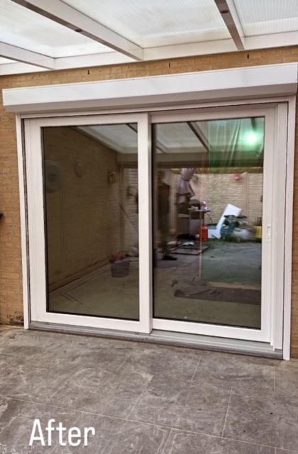 Witte, omlijste schuifdeuren van glas met oprolbaar rolluik, buitenomgeving met zichtbare weerspiegeling van het interieur.