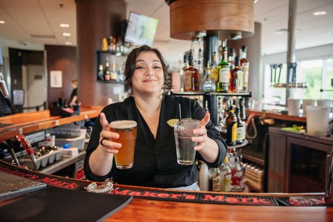 A woman is sitting at a bar holding two drinks.