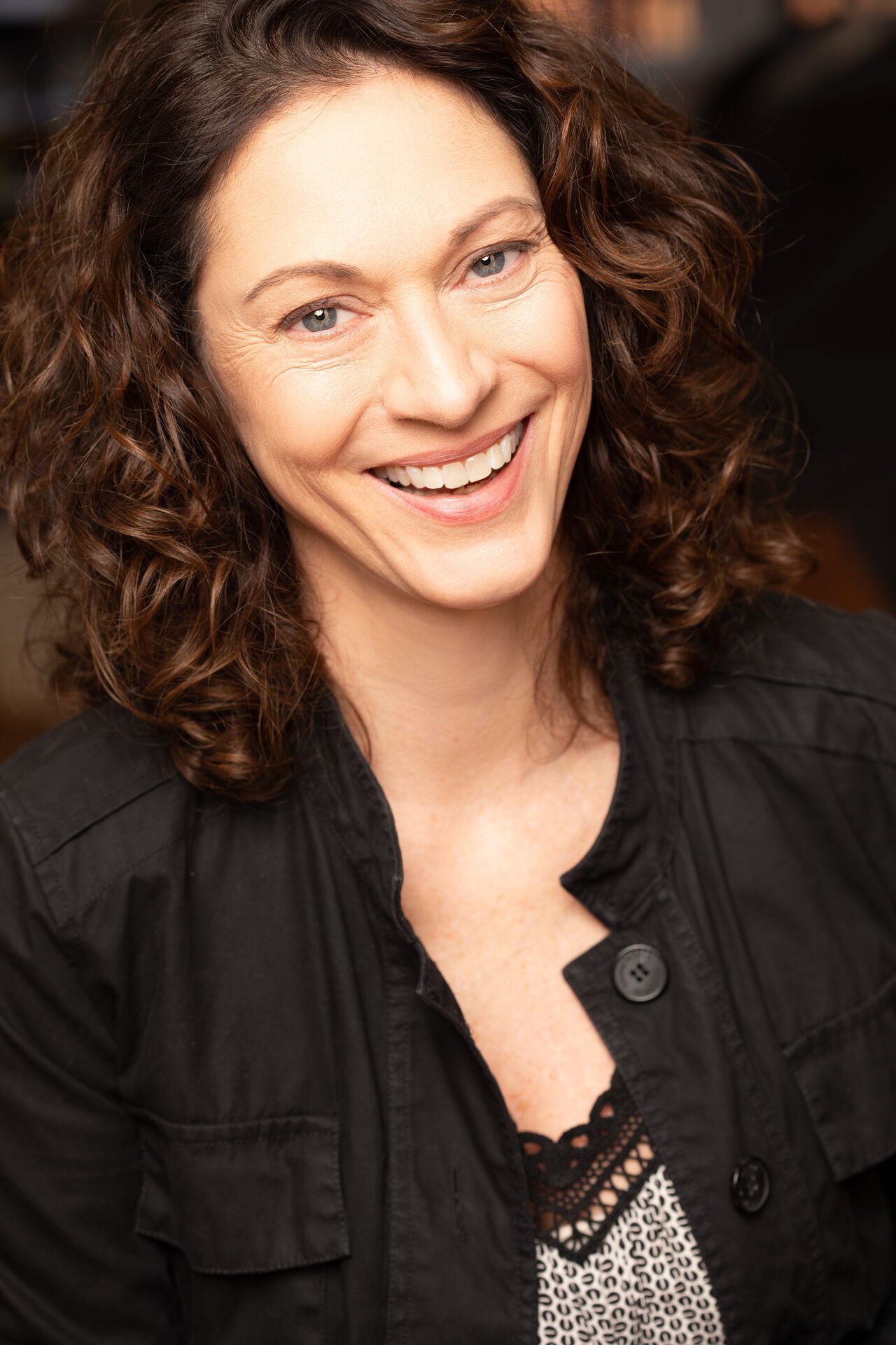 A woman with curly hair is smiling and wearing a black jacket.