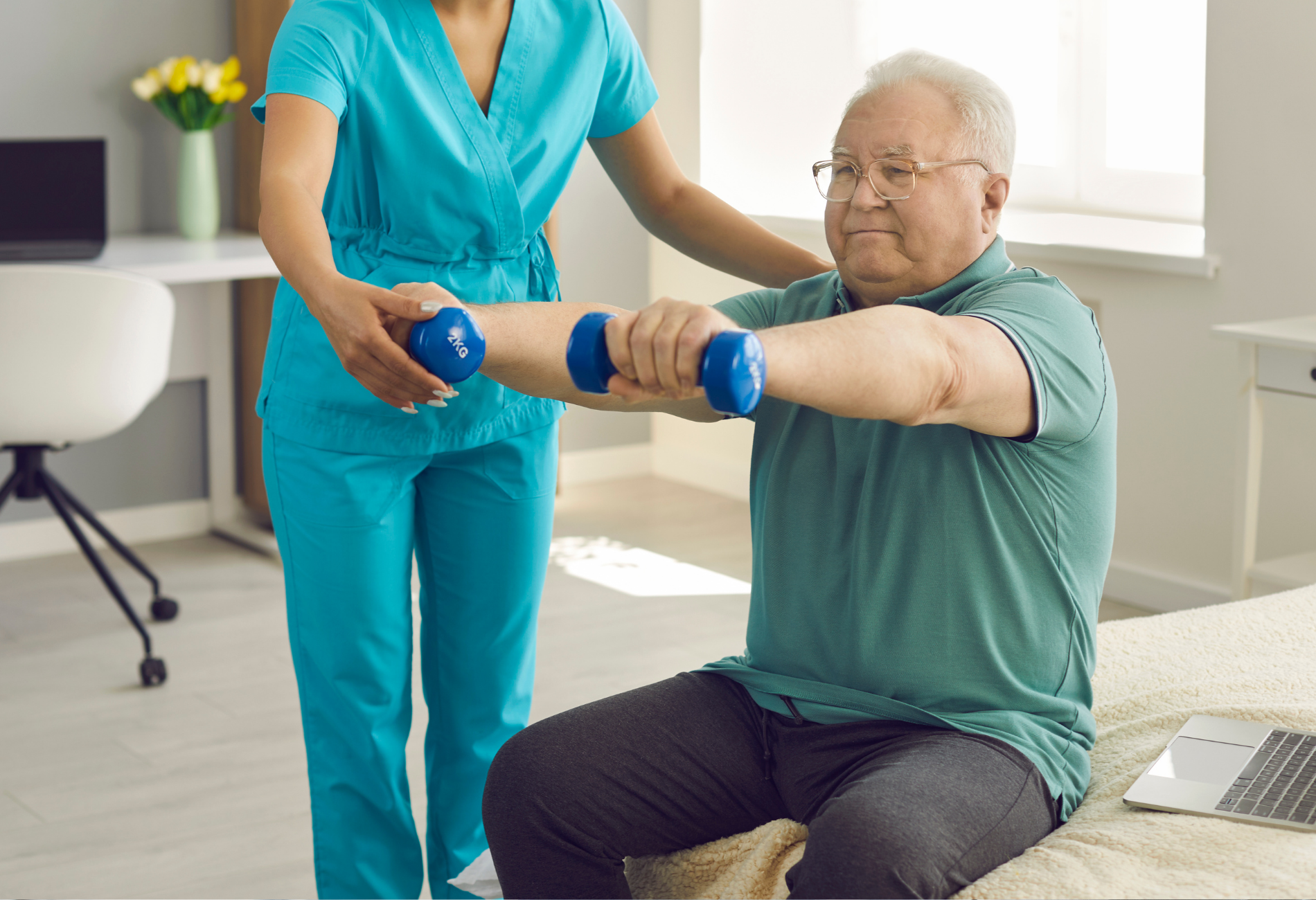 Physical therapist assisting a seated person with dumbbell exercises; indoors, wearing scrubs.