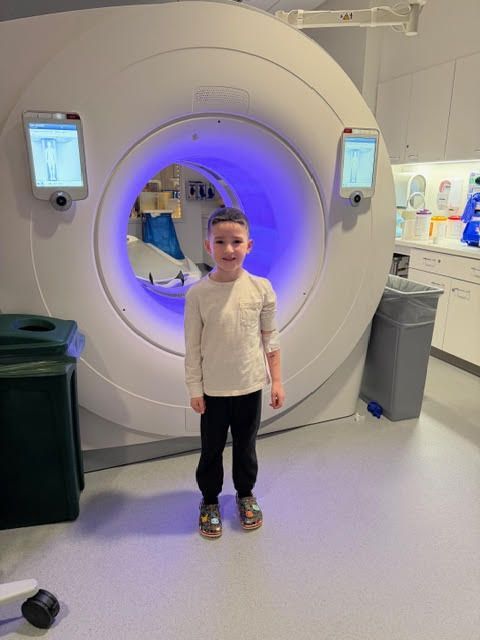 A person stands in a medical imaging suite in front of a large, circular CT scanner with glowing blue interior lighting.
