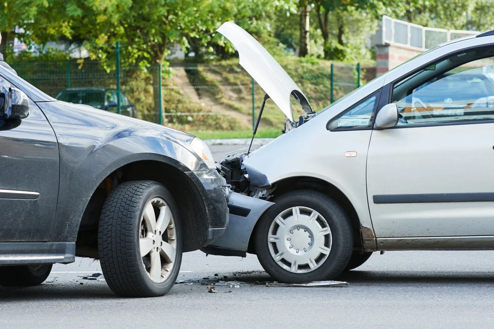 Two cars after a collision: gray car front-end damaged, silver car hood open, damage to bumper.
