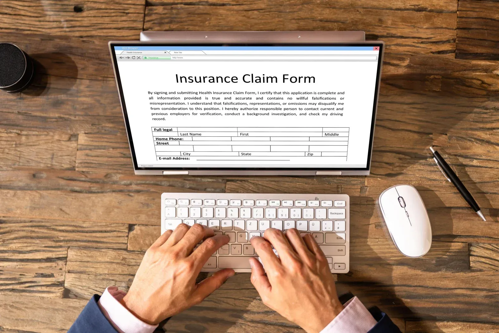 Hands typing on a keyboard, filling out an insurance claim form on a laptop.