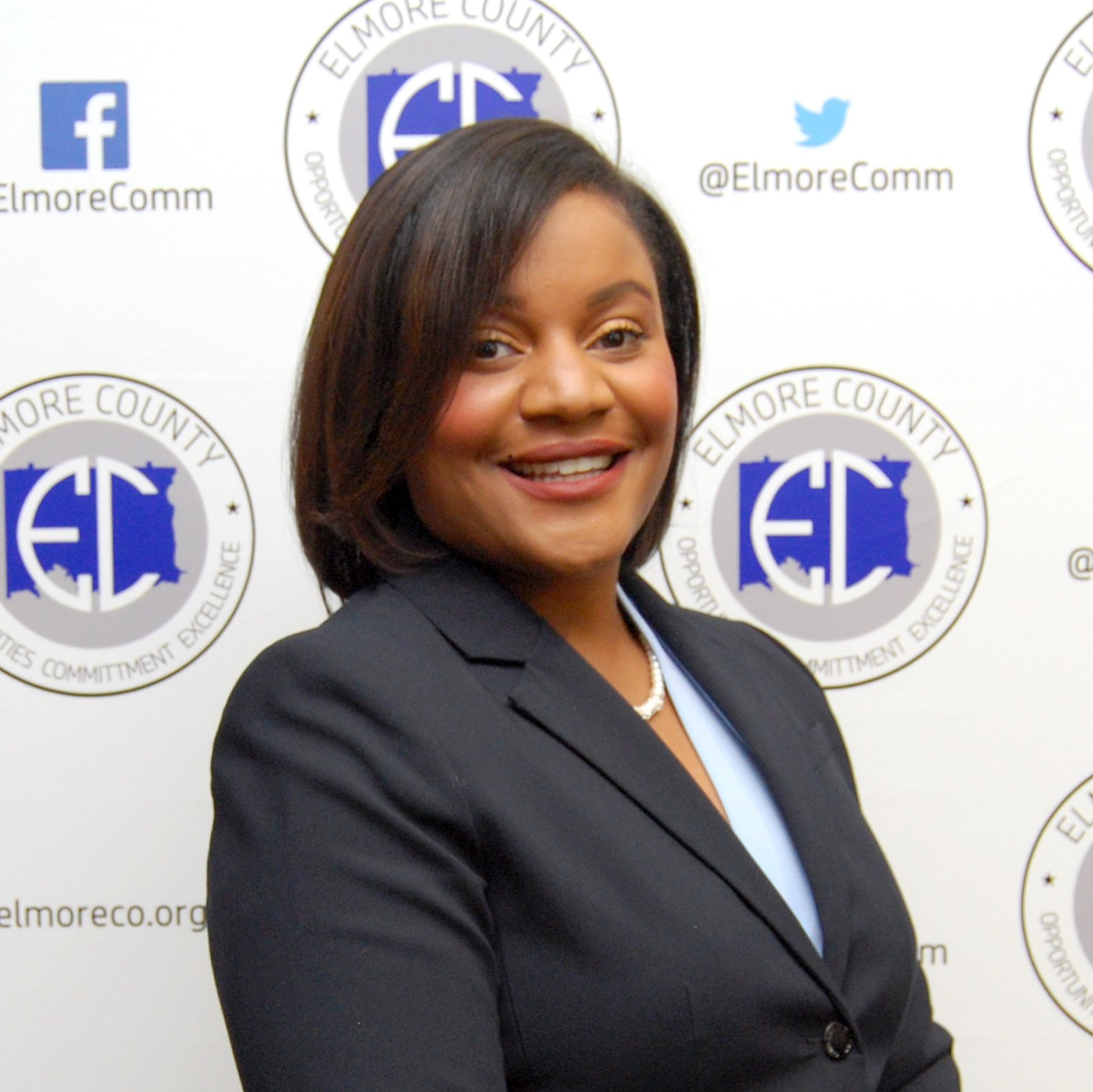 Woman in a dark suit smiles in front of a backdrop with 