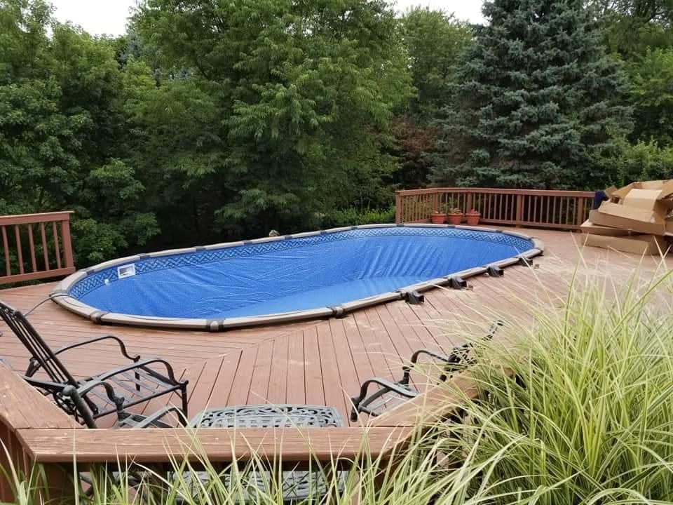 A large oval swimming pool is sitting on top of a wooden deck.