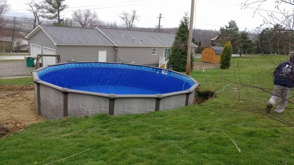 A man is standing next to a swimming pool in a backyard.