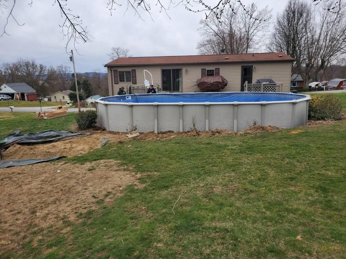 A large swimming pool is sitting in the grass in front of a house.