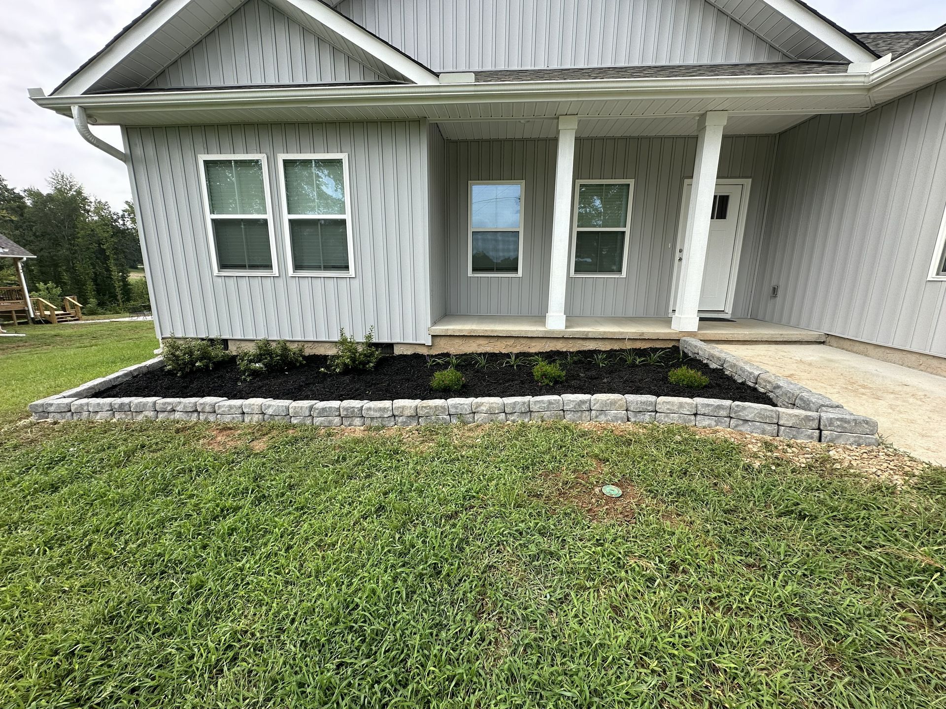 Front view of a gray house with white trim, porch columns, windows, and a stone-edged garden bed.