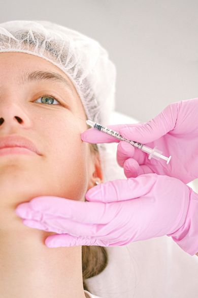 Gloved hands inject filler into a woman’s cheek in a clinical setting