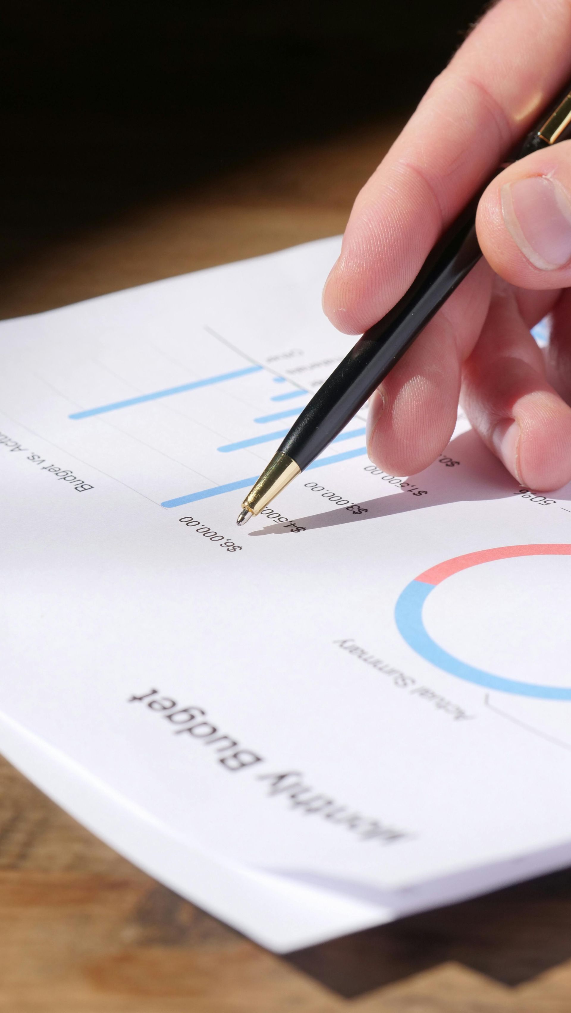 Hand holding a pen over a printed report with charts and graphs on white paper